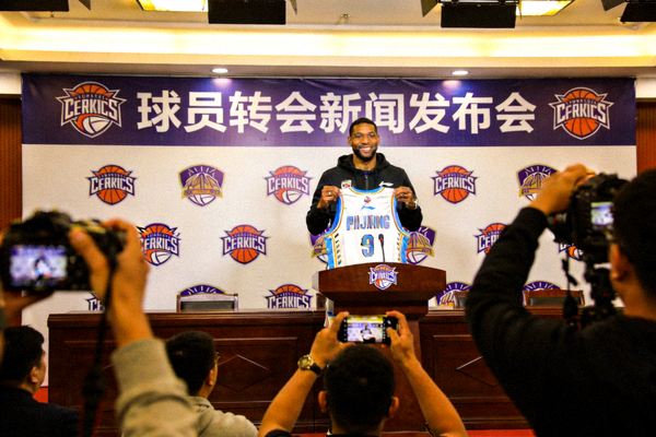 篮球球员转会新闻发布会现场，球员手持新球队球衣